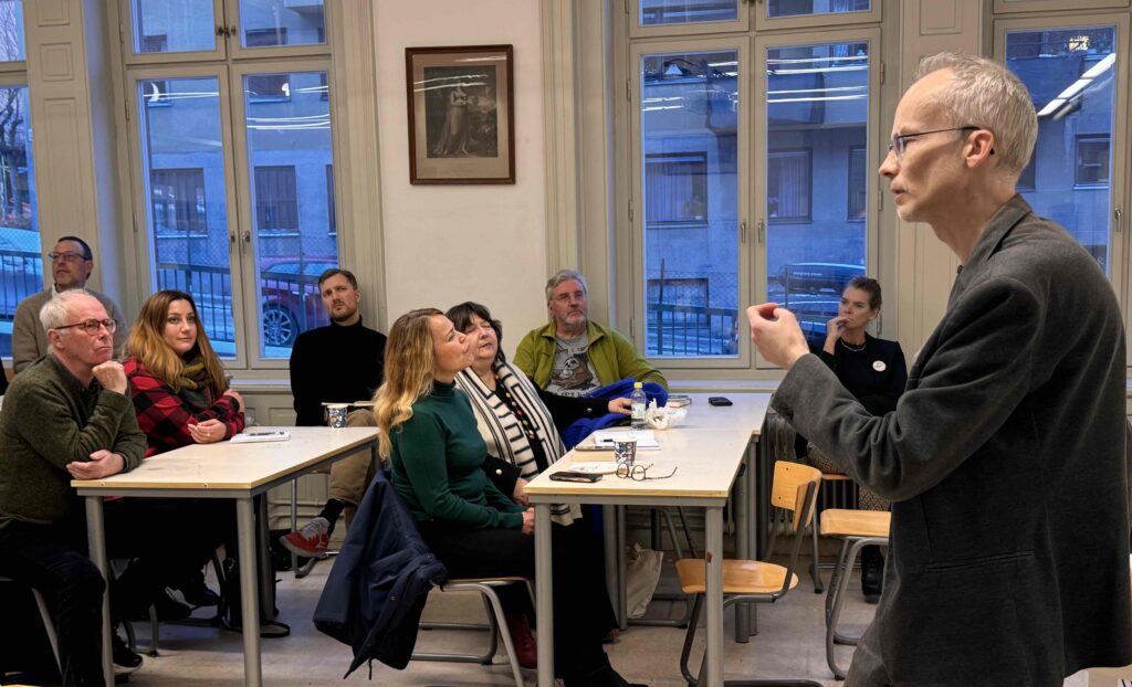 Mathias Tistelgren, filosofisk praktiker och medlem i SSFP, håller i en workshop. Han talar inför en grupp som sitter i bänkar på rad framför honom.