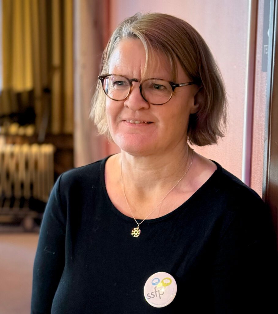 Cecilia Brisander, medlem i SSFP, som är med och arrangerar årets Världsfilosofidag. Hon står framför ett bord och ses i närbild.